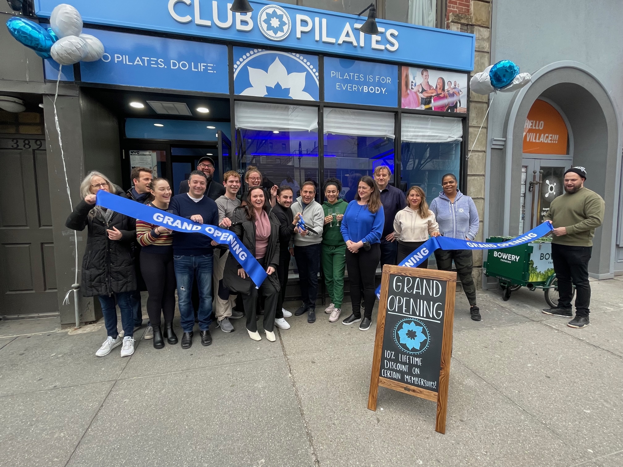 Ribbon cutting west village - photo of Club Pilates West Village Staff holding a ribbon of their grand opening in front of their store